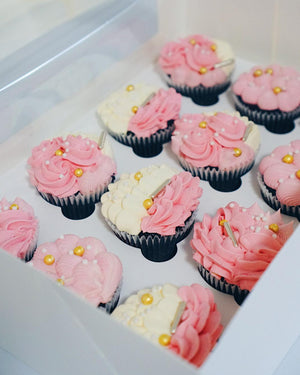 Box of cupcakes with pink and white frosting and yellow candies.