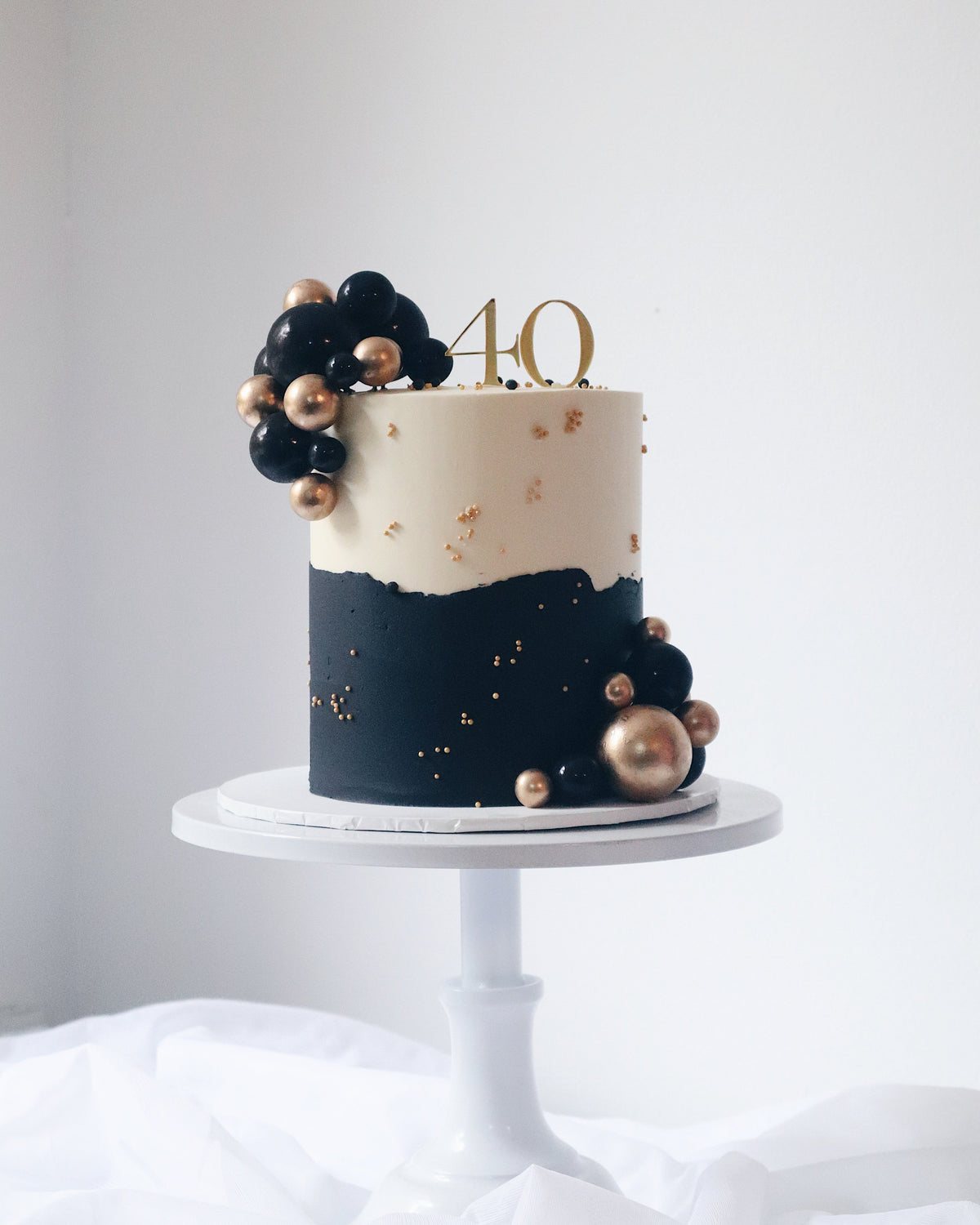 Navy and white cake with gold decorations on a white stand against a light gray background