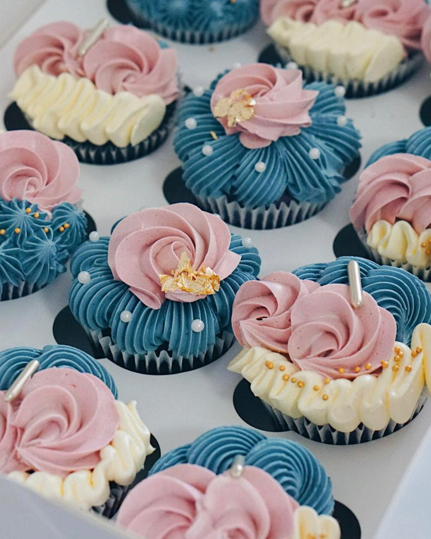 Decorative cupcakes with pink, blue, and white frosting on a white surface.