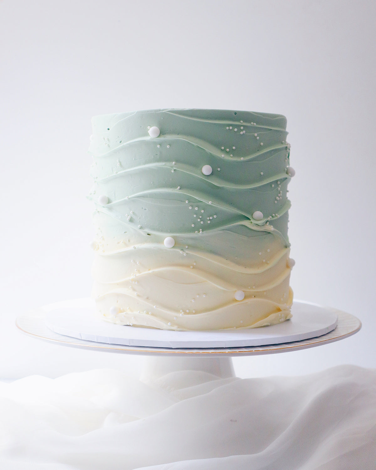 Two-tiered cake with wavy green and beige design on a white background