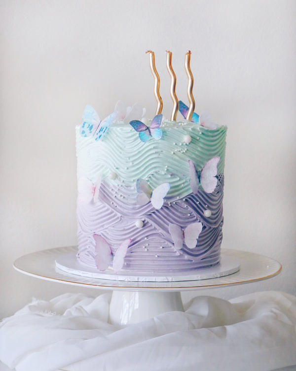 Decorative cake with wavy icing pattern and butterfly decorations on a white stand.