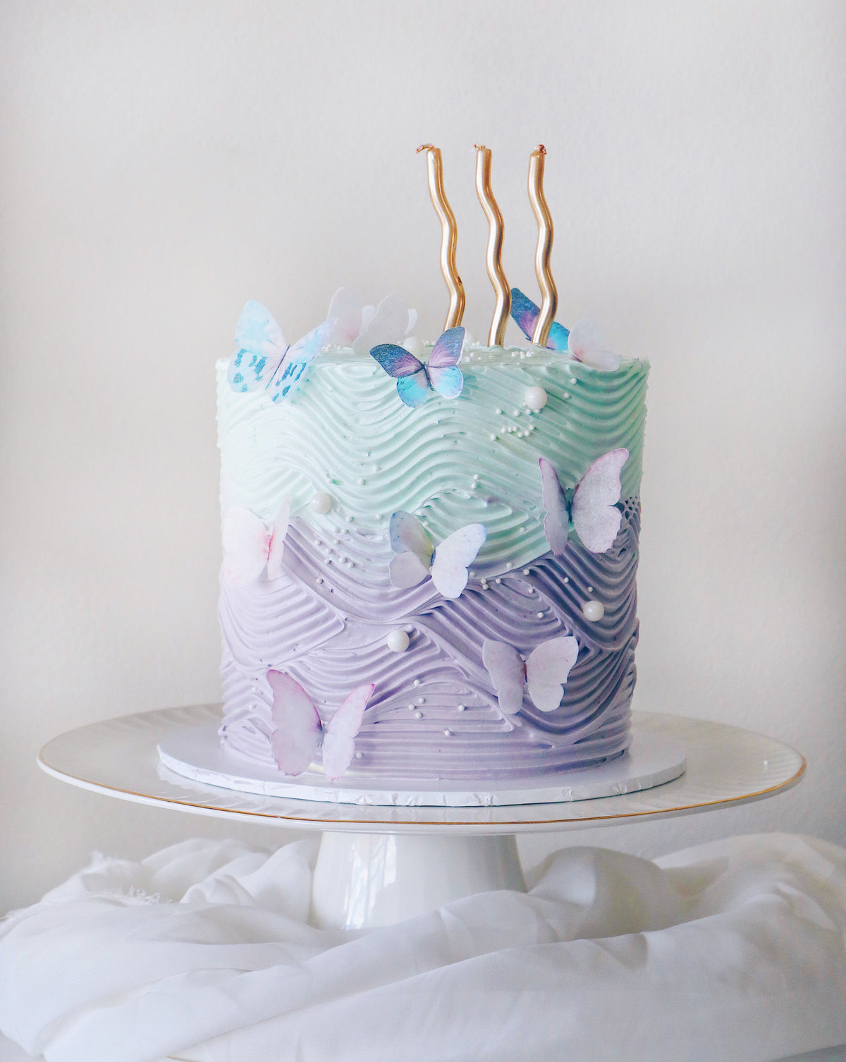 Decorative cake with wavy icing pattern and butterfly decorations on a white stand.