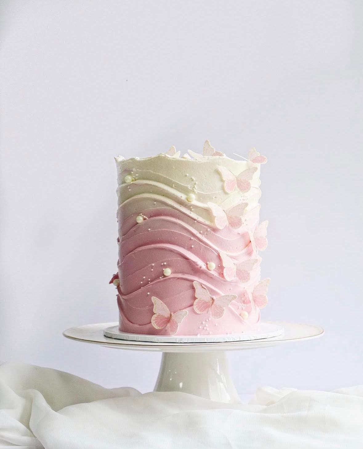 Pink and white ombre cake on a white stand with a white background