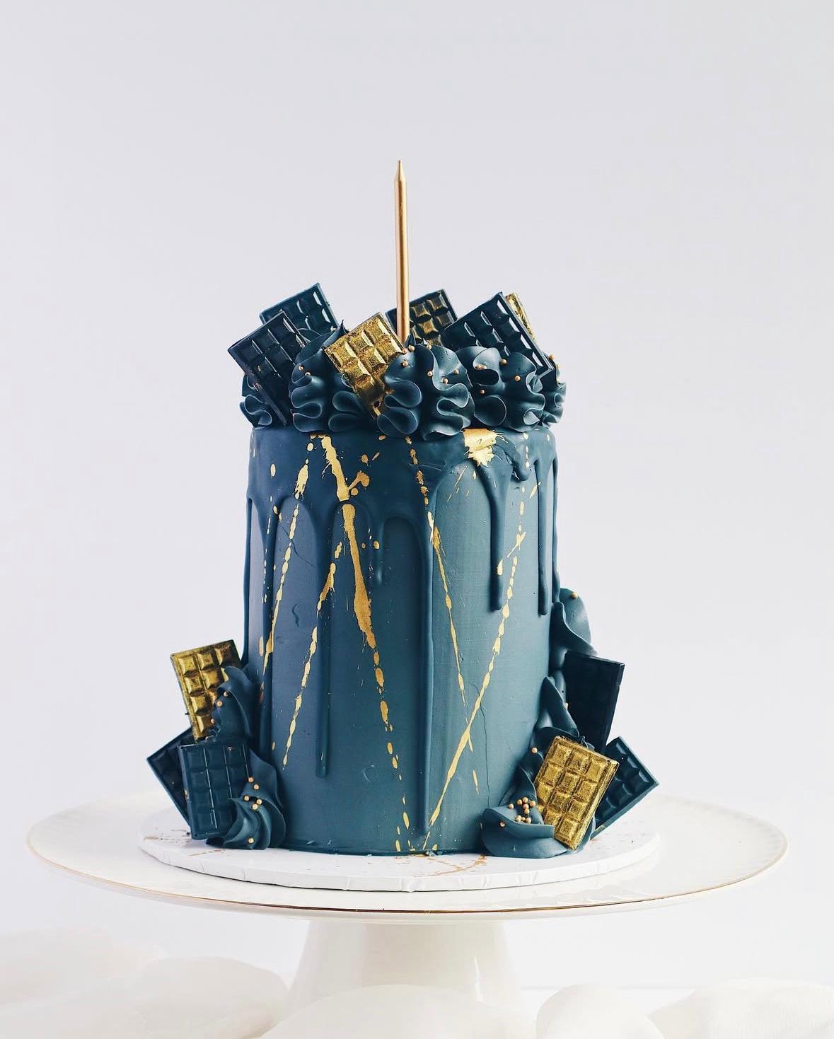 Decorative cake with blue and gold elements on a white stand