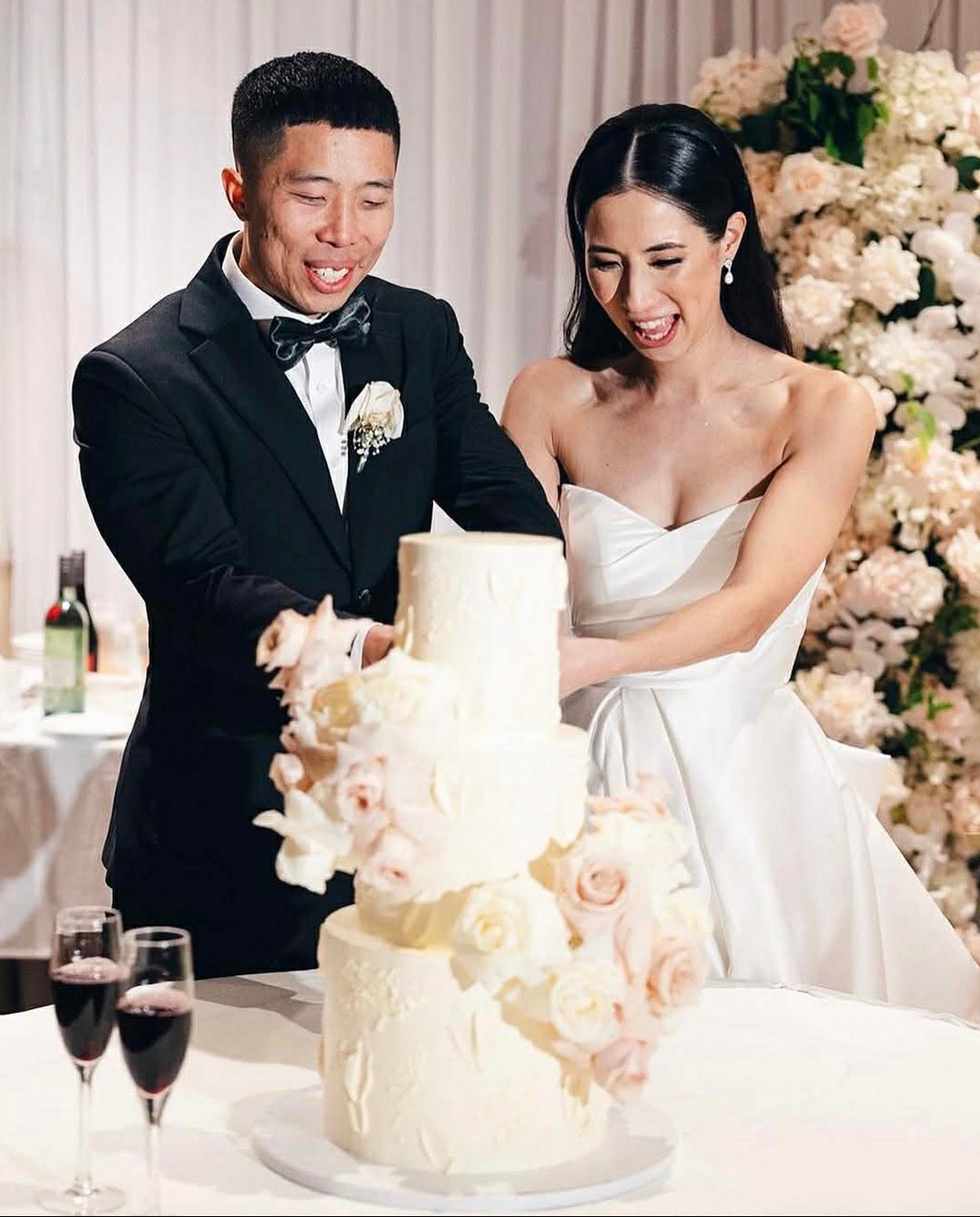 Couple cutting a wedding cake with floral decorations in the background