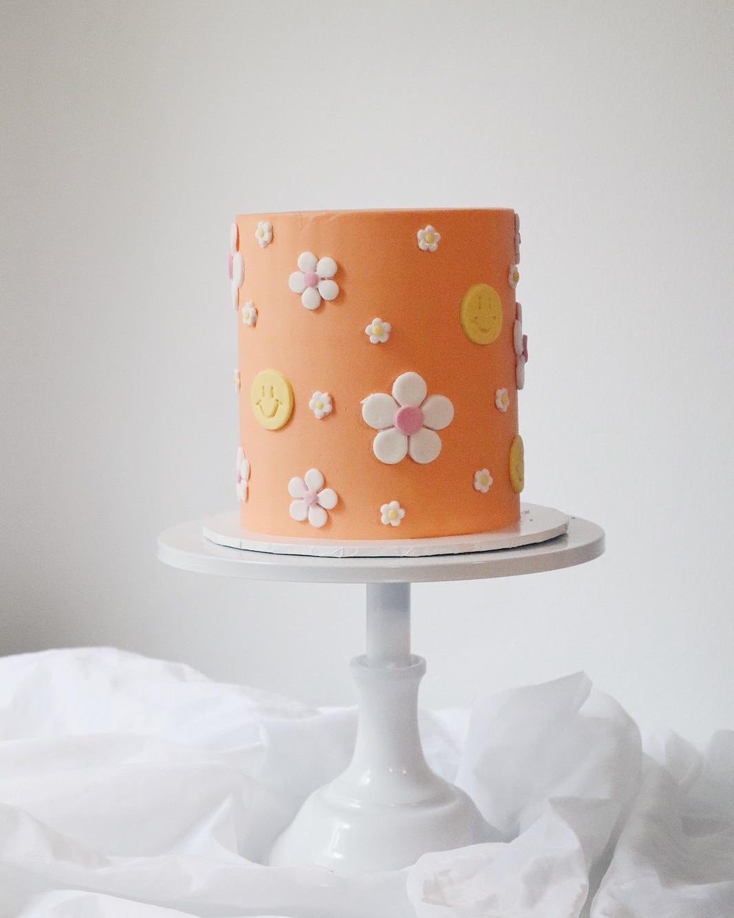 Orange cake with floral decorations on a white stand against a light gray background