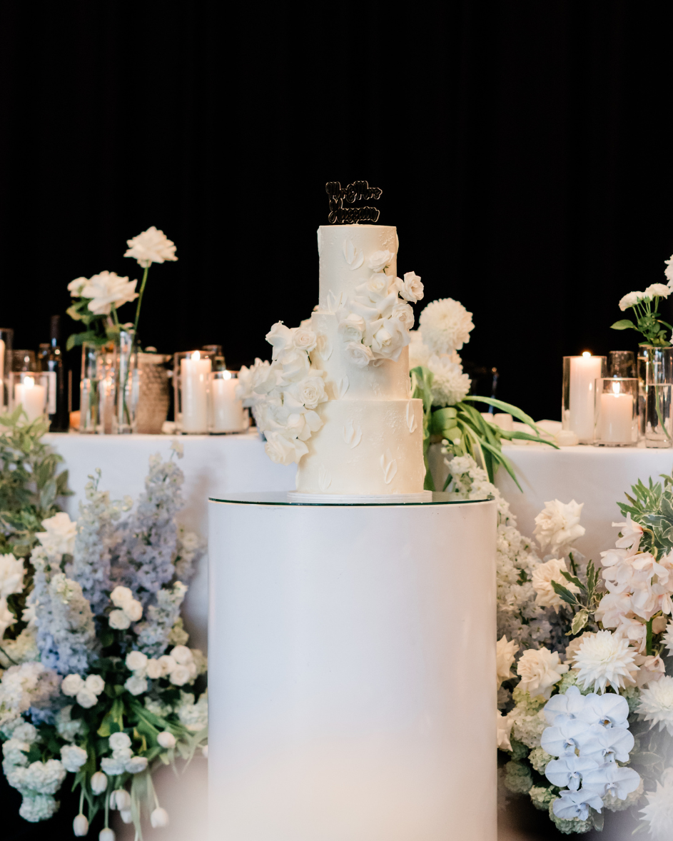 White wedding cake with floral decorations on a table with flowers and candles.