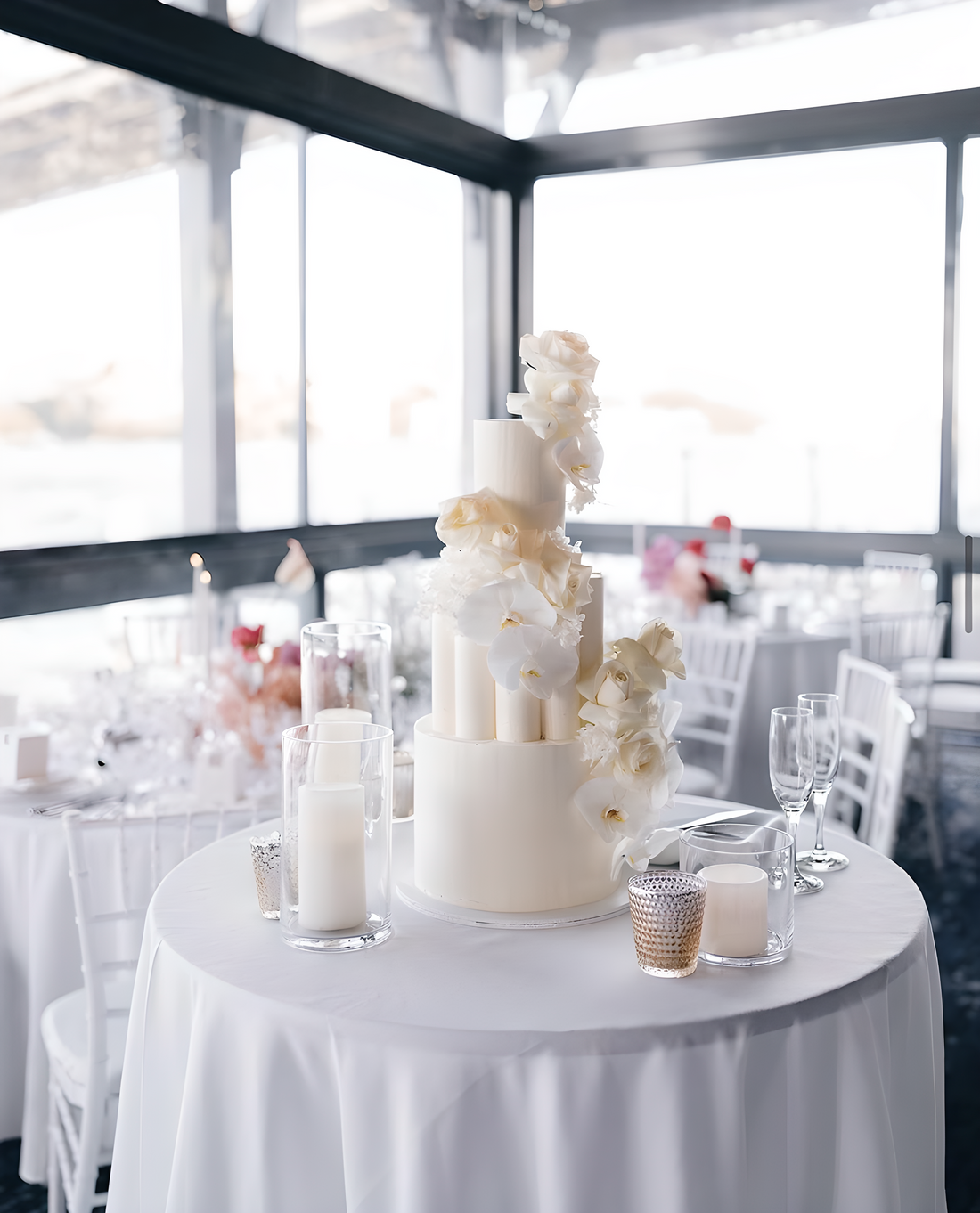 White wedding cake on a round table with candles and flowers in a large room.