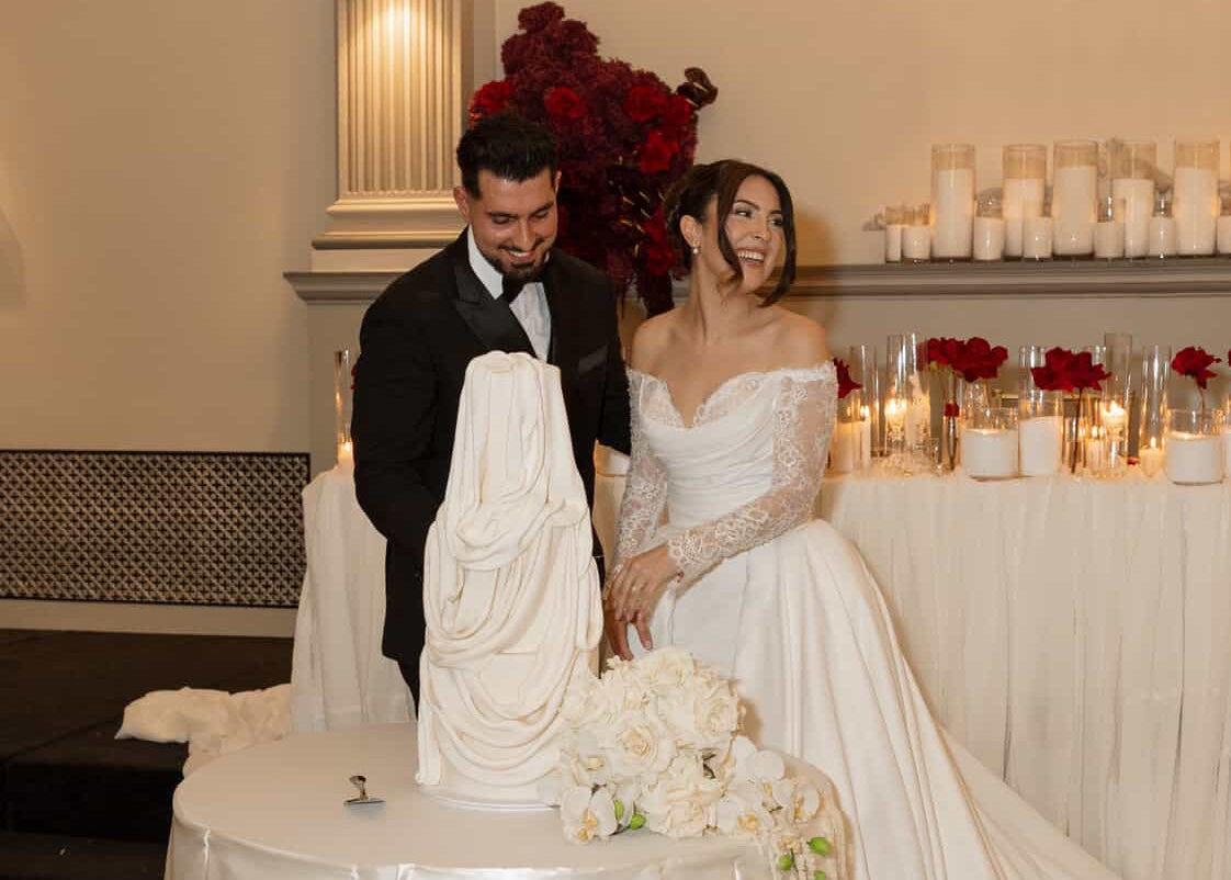 Couple cutting a wedding cake in a decorated room with candles and flowers.