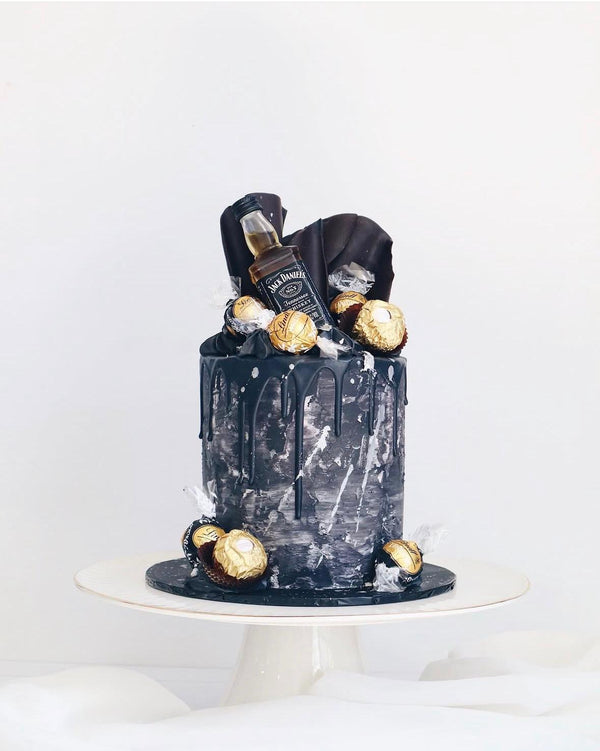 Black cake with Jack Daniel's bottle and gold balls on a white background