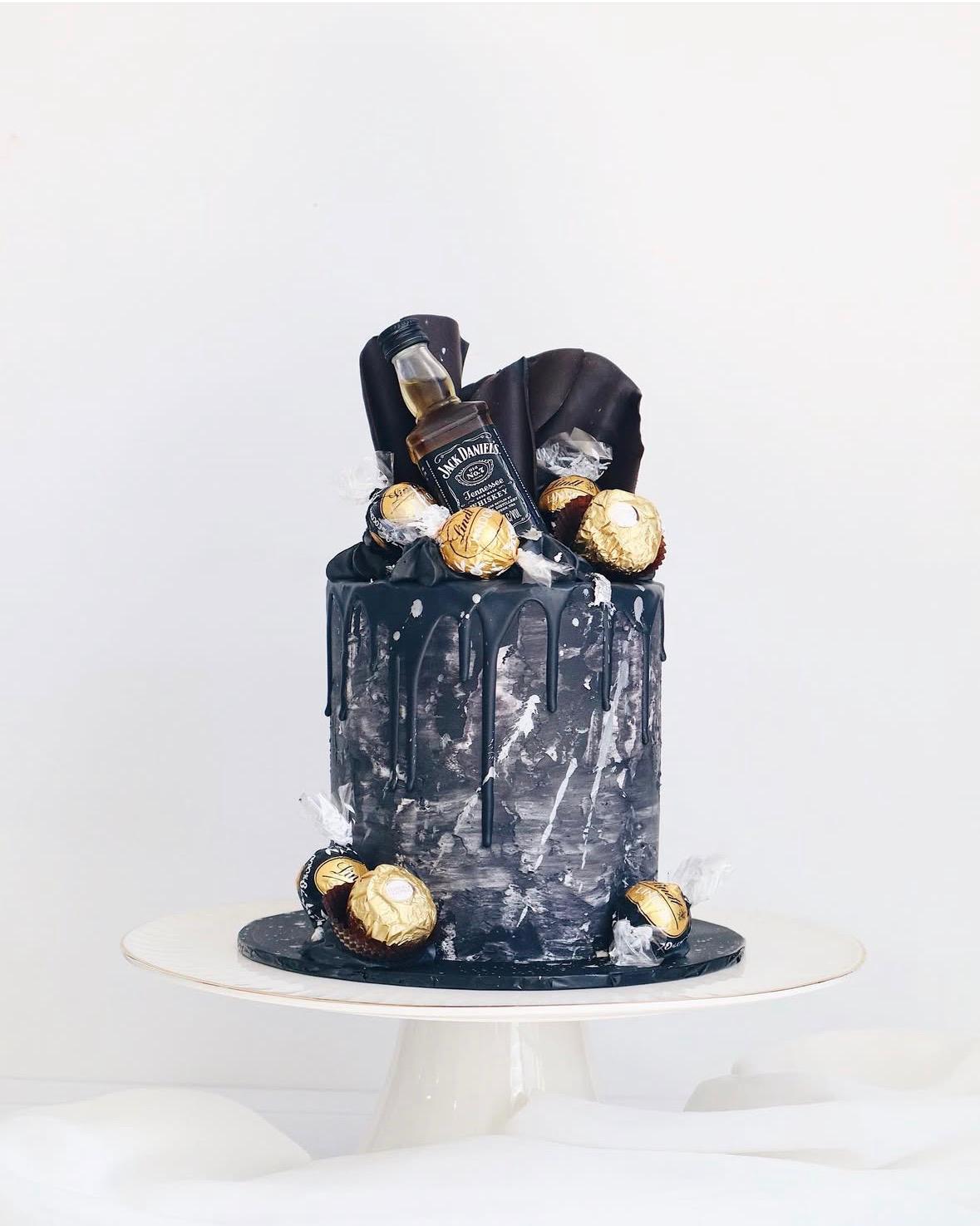 Black cake with Jack Daniel's bottle and gold balls on a white background