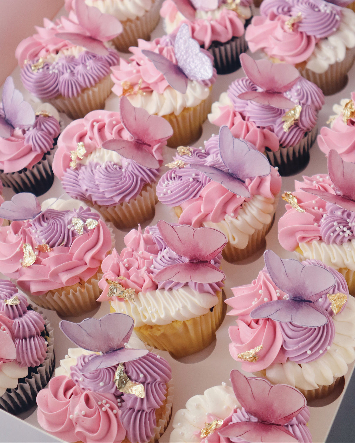 Decorative cupcakes with pink and purple frosting and butterfly decorations on a white surface.
